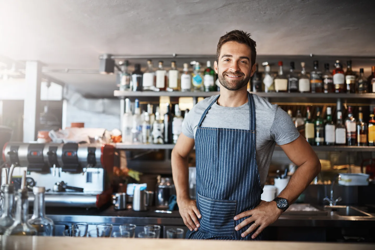 A person in a striped apron standing behind a counter, with spirits bottles on the shelving behind them — liquor store insurance in Delaware