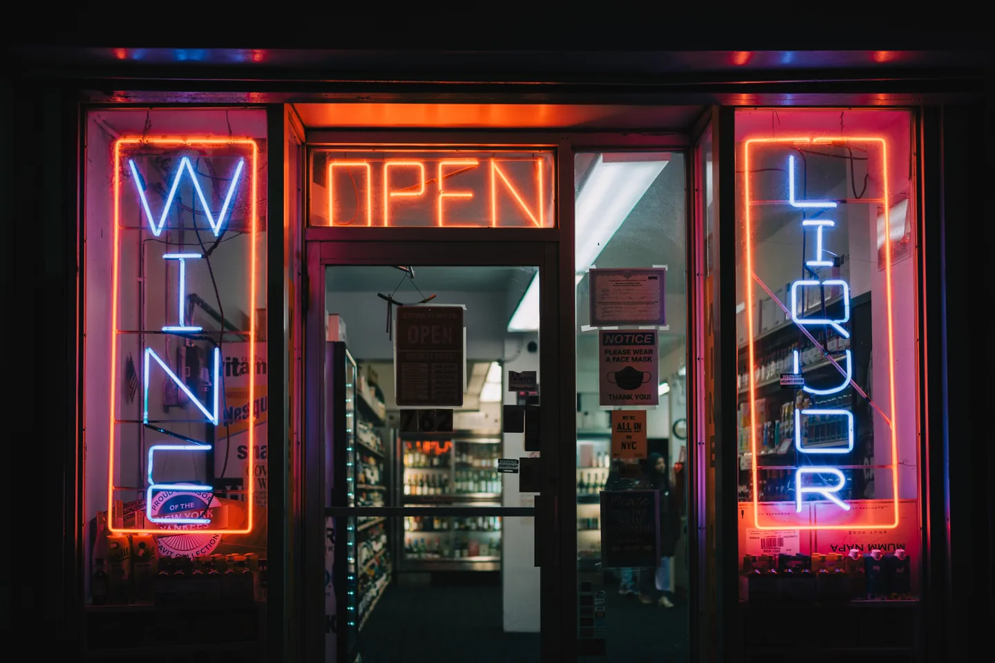 A shopfront at night, with neon wine, open and liquor signs lit beside an open doorway — liquor store insurance in Ohio