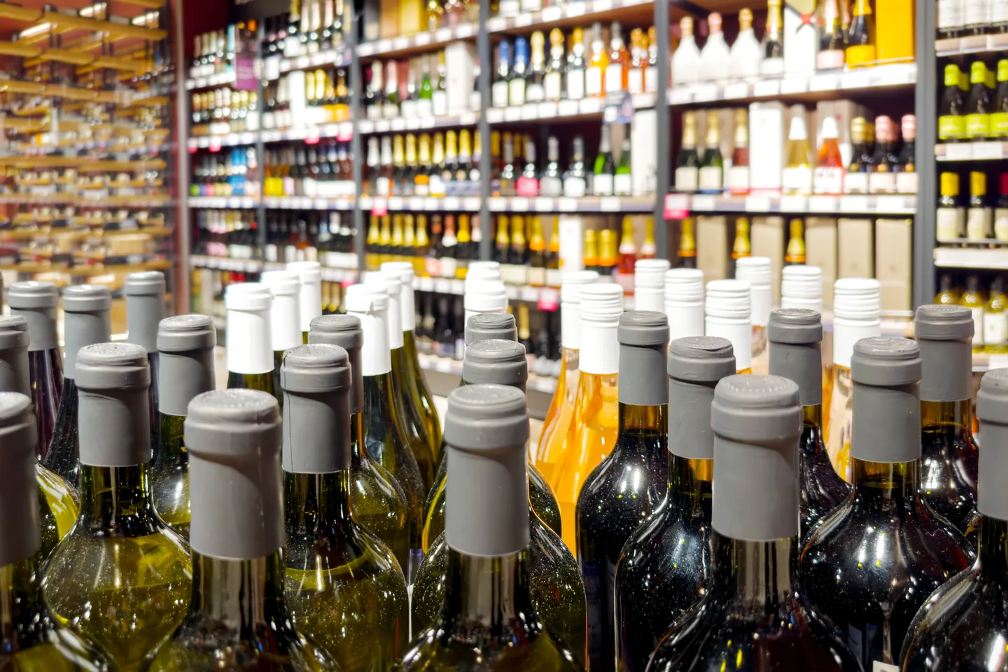 Rows of screwcapped wine bottles in the foreground with stocked store shelving out of focus behind — liquor store insurance in Wyoming