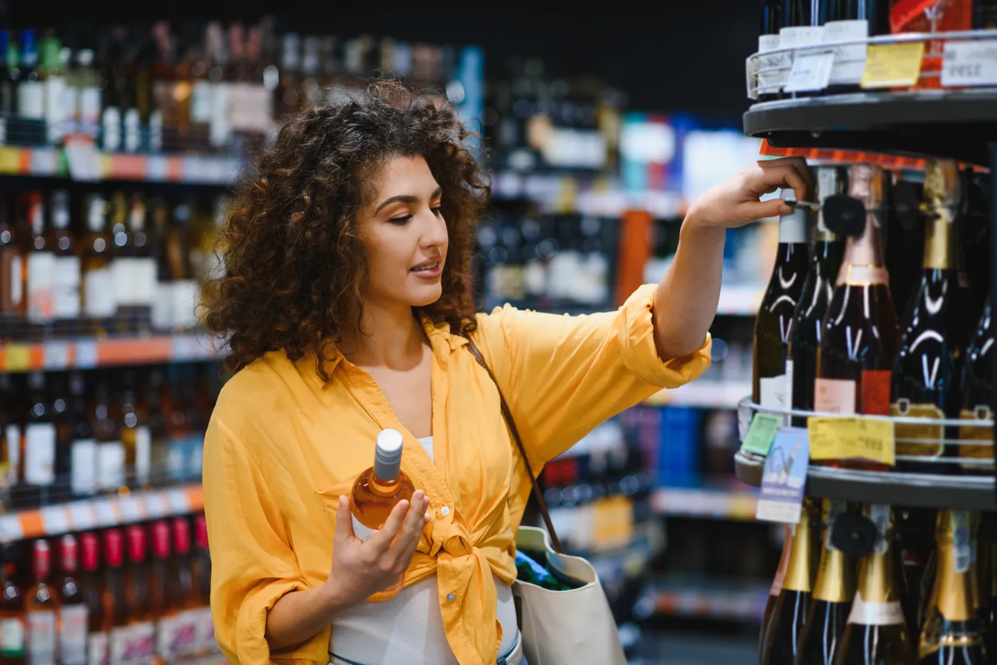 A shopper holding one bottle and reaching for another from a round sparkling wine display — liquor store insurance in Alabama