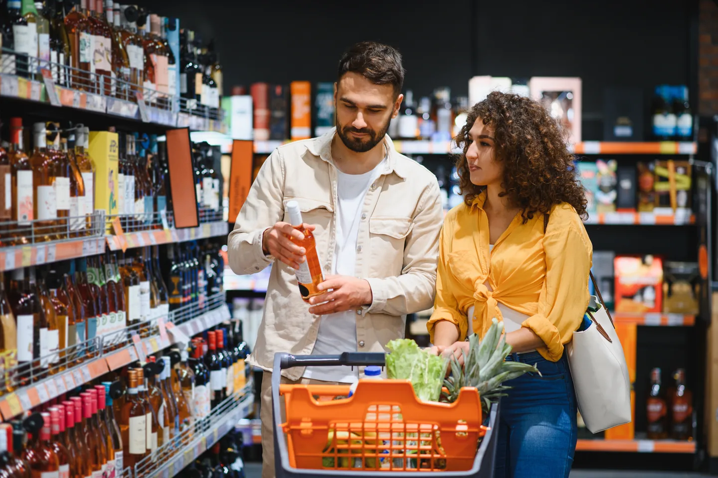 Two shoppers looking together at a bottle taken from the shelf, a trolley of groceries in front of them — liquor store insurance in Kentucky